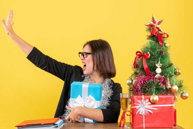 树情绪混乱的商务女士 穿着西装 戴着眼镜 拿着礼物给别人打电话 坐在一张桌子旁 桌子上放着一棵圣诞树情绪人礼物