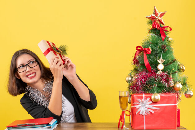 庆典一位穿着西装 戴着眼镜 拿着礼物 坐在办公室里一棵圣诞树旁的商务女士吓了一跳时尚漂亮眼镜