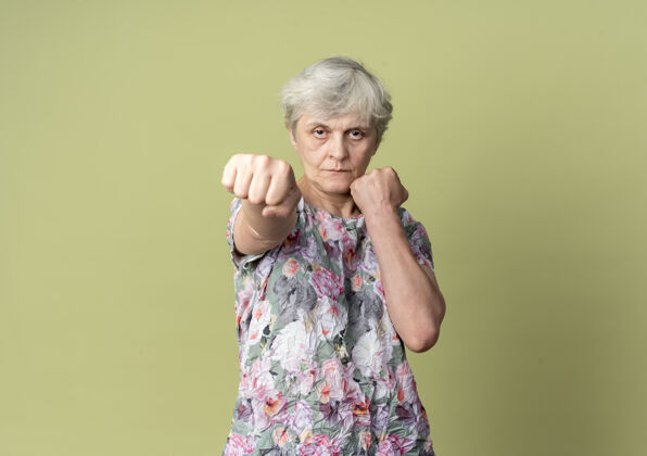 女人自信的老妇人把拳头放在橄榄绿的墙上 随时准备出击重拳信心绿色