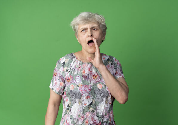 自信自信的老妇人把手紧握在嘴边 假装在绿色的墙上叫一个孤立的人绿抱嘴