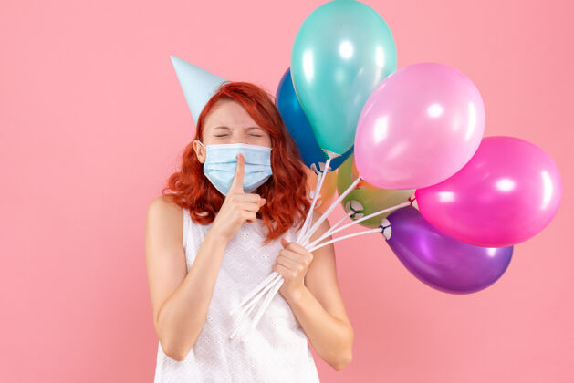 快乐正面图年轻的女性手持彩色气球在面具上浅粉色举行年轻女性病毒