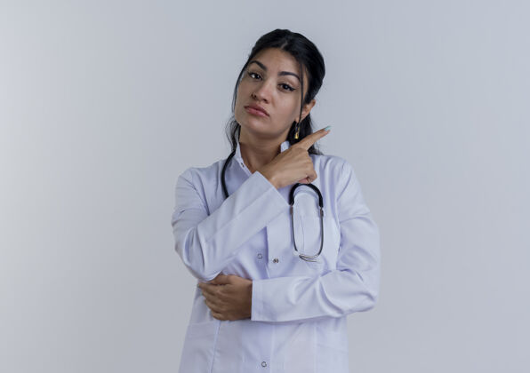 女人年轻的女医生穿着医用长袍 用听诊器指着隔离的一边看着医生听诊器指尖