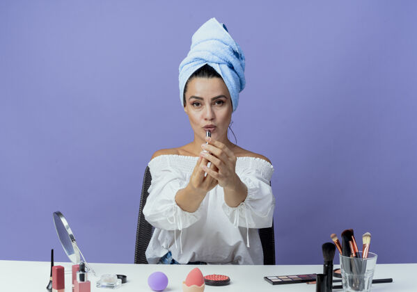 工具自信漂亮的女孩裹着发巾坐在桌子上 手里拿着化妆工具 手里拿着紫红色的隔离墙漂亮毛巾紫色