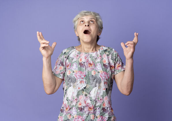 老兴奋的老妇人交叉着手指 孤零零地看着紫色的墙上老紫色女人