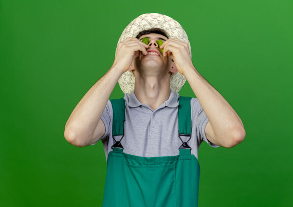 绿色高兴的年轻男园丁戴着园艺帽 眼睛被打破辣椒隔离在绿色背景与复制空间男性请花园