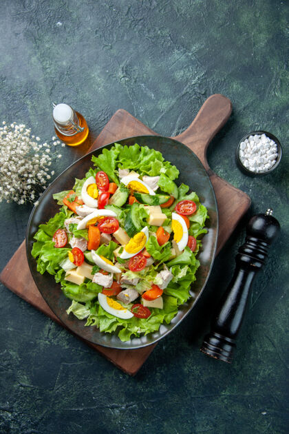 新鲜俯瞰美味的沙拉与许多新鲜的原料在木制砧板上盐油瓶黑绿色混合色的背景切割炊具食物