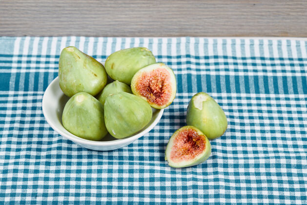 切片绿色无花果在一个白色的碗和一个木制的桌子上与蓝色桌布高品质的照片热带水果健康