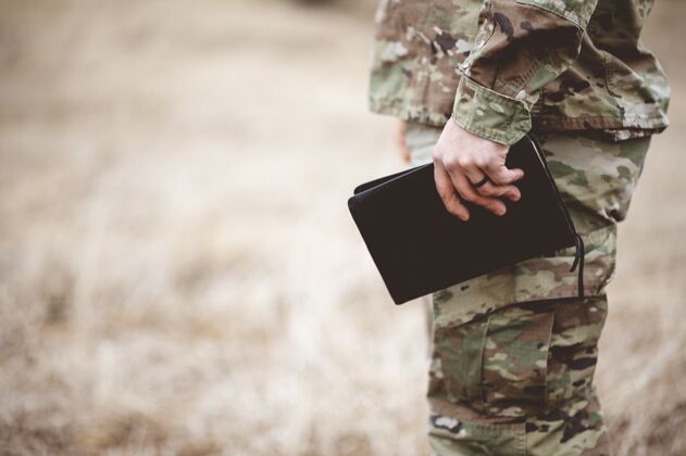男性一个年轻士兵拿着一本圣经在田野里的浅焦镜头战争保护战士
