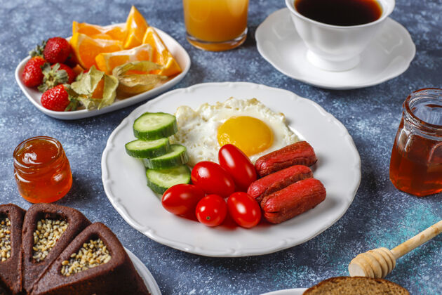 新鲜早餐盘子里有鸡尾酒香肠 煎蛋 樱桃番茄 糖果 水果和一杯桃子汁食物蔬菜营养