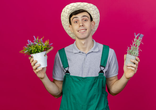 粉色微笑着的年轻男园丁戴着园艺帽 手里拿着粉红色背景上的独立花盆 还有复制空间男性复制空间