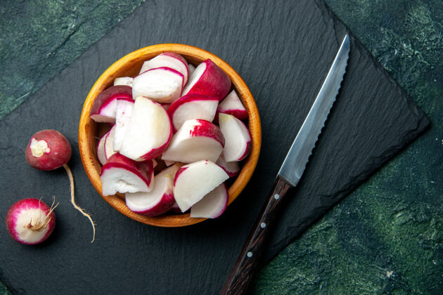 刀在绿色和黑色混合色背景上的深色切割板上 在碗和刀中近距离观看整个和切碎的新鲜萝卜 并提供自由空间板黑暗关闭
