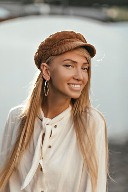模型快乐迷人的女人穿着时髦的棉质衬衫 戴着时髦的棕色帽子 笑容满面 心情愉快地走在外面人成人人