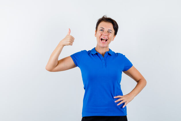 人成熟的女人在蓝色t恤上竖起大拇指 看起来很自信 正面视图微笑柔软拇指