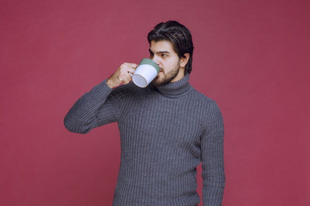 男性穿灰色毛衣的男人从杯子里喝咖啡聪明人服装