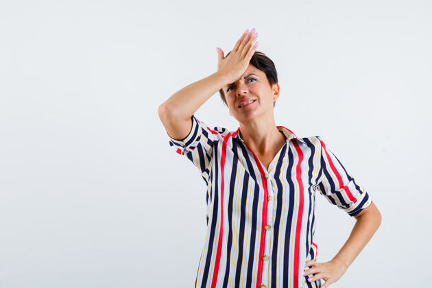 健康成熟的女人把一只手放在额头上 一只手放在腰上 穿着条纹衬衫 看起来很烦躁前视图微笑活跃姿势