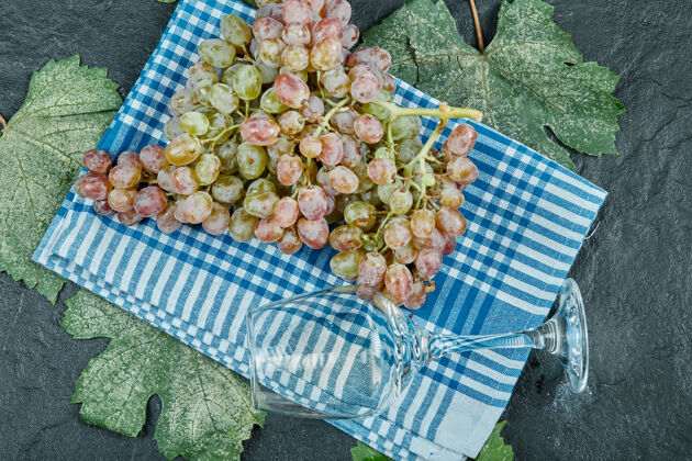 多汁一束红葡萄和一个酒杯放在蓝色的桌布上 上面有叶子高质量的照片食物成熟自然