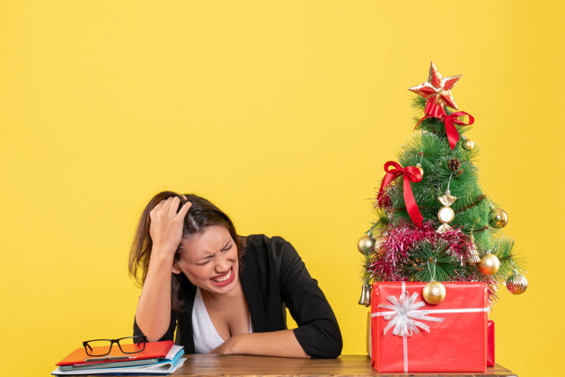 新郎在黄色的办公室里 一个穿着西装的愤怒的年轻女人站在装饰过的圣诞树旁年轻女子黄色人