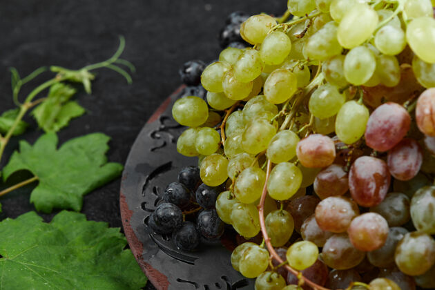 陶瓷一堆混合的葡萄放在一个有叶子的陶瓷盘子里高质量的照片水果一串成熟