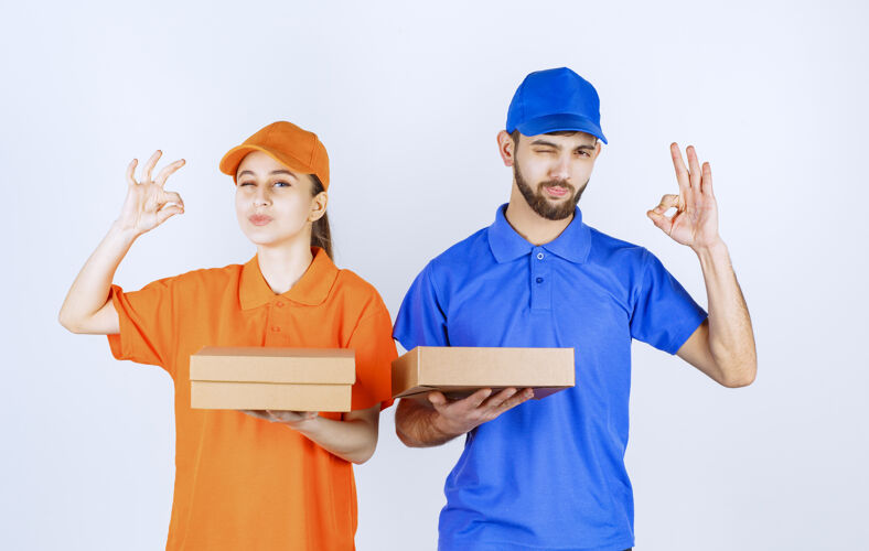 男性身穿蓝黄制服的男女快递员手持纸板外卖盒和购物包 并展示满意手势工人快递产品