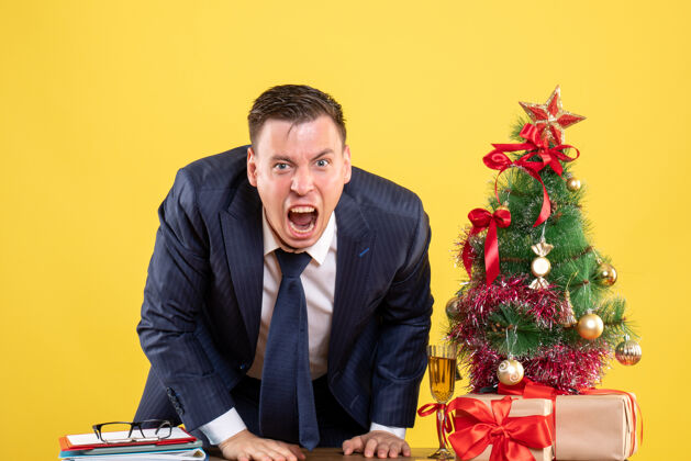 新郎前视图愤怒的商人站在圣诞树旁 黄色背景上呈现公司女业务员圣诞节