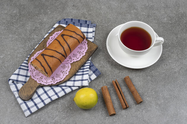 甜点甜甜的卷蛋糕 一杯茶和肉桂棒放在大理石表面小吃蛋糕肉桂