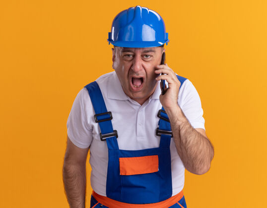 某人愤怒的成年建筑工人穿着制服对着电话里被隔离在橙色墙上的人大喊大叫人感觉衣服