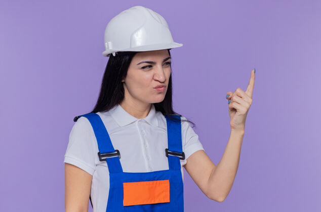 制服身穿施工制服 头戴安全帽的年轻建筑工人一边困惑地看着一边 一边不高兴地举起手臂建筑站在一边建设者