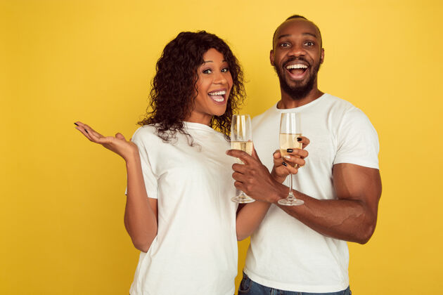 立场喝香槟情人节庆祝 快乐的非洲裔美国夫妇隔离在黄色工作室背景下人类情感的概念 面部表情 爱情 关系 浪漫的节日非洲团结约会
