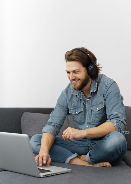 笔记本电脑带着耳机的满脸笑容的男人活动室内全镜头