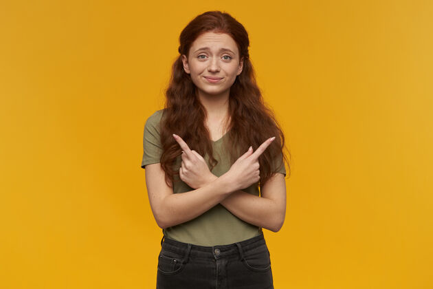 姜可爱 积极向上的女人 长着一头姜黄色的头发穿着绿色的t恤人和情感的概念不确定地指向复制空间的两边被隔离在橙色的墙上成人20多岁学生