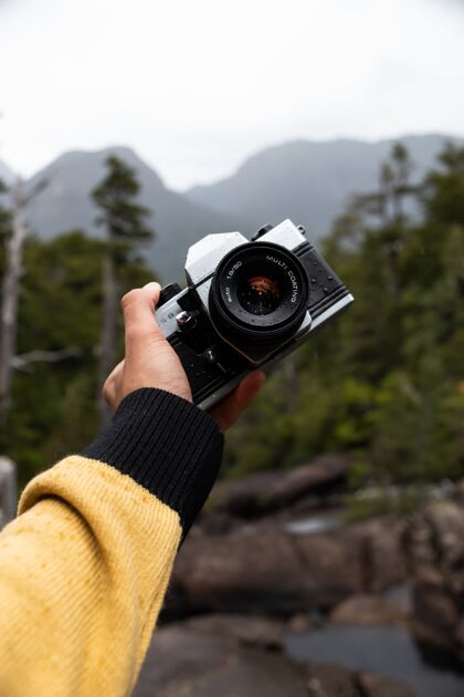 男垂直拍摄的是一只手拿着专业相机与森林的男性人森林手