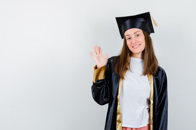 年轻女毕业生身着学院服挥手致意的画像 正望着欢快的前景色Cap长袍欢呼