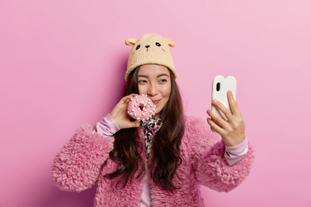 甜点相当快乐的韩国女孩与新鲜出炉的甜甜圈合影 自拍肖像 不健康饮食 在社交网络上分享照片面包房女士美味