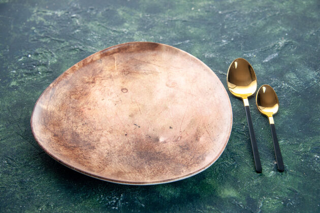 深色的正面图棕色盘子和金色勺子在黑暗的背景上勺子食物晚餐