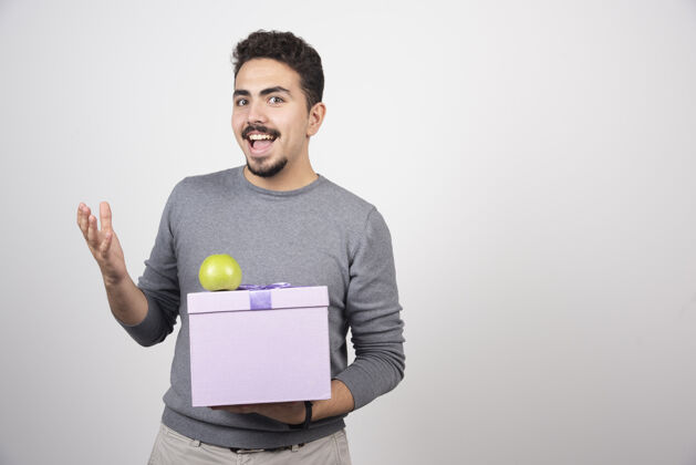 苹果快乐的男人手里拿着一个紫色的盒子和一个绿色的苹果礼物人类男人