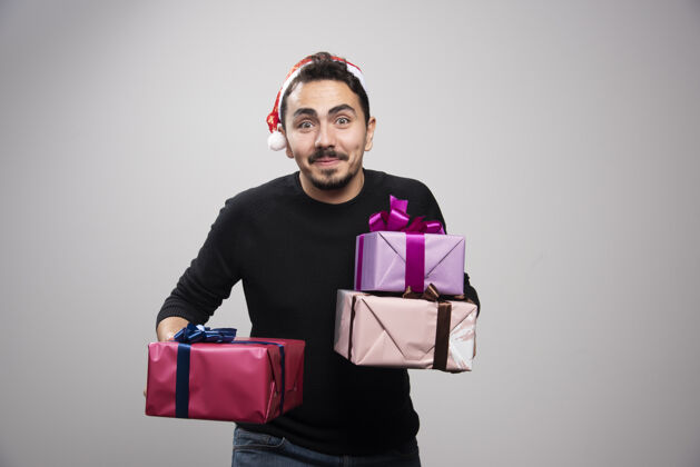 肖像一个年轻人拿着礼品盒在灰色的墙上站礼物模特