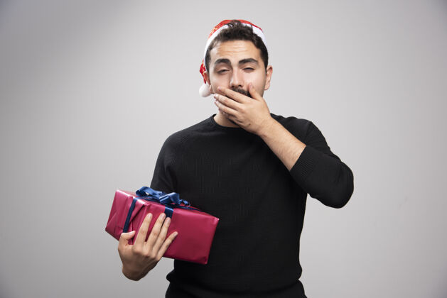 站一个年轻人拿着一个礼品盒在灰色的墙上圣诞礼物圣诞老人