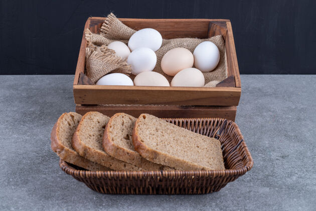 面包房柳条篮子的黑面包和木箱的生鸡蛋放在石头上食品小吃吐司