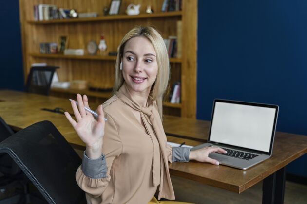 笔记本电脑一个微笑的女人在办公室里挥手 一边用笔记本电脑就业工作空间工作