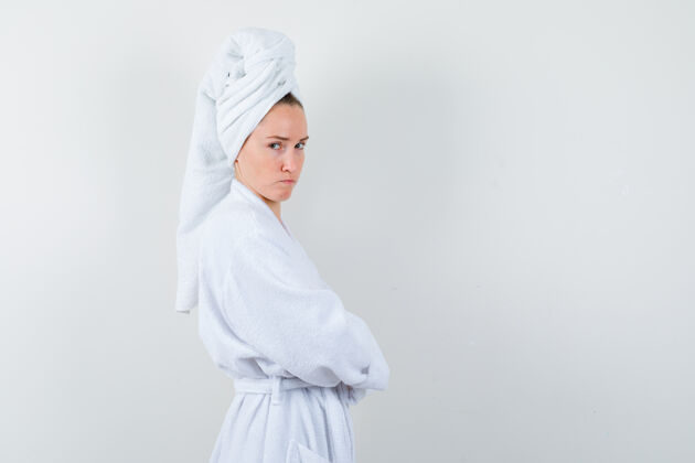 床年轻女子交叉双臂站在白色浴衣 毛巾和失望的样子漂亮手臂女性
