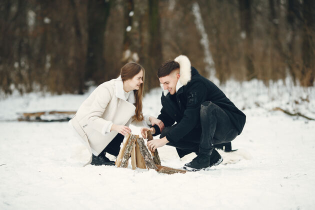 篝火生活方式拍摄的一对夫妇在雪林人们在户外度过寒假人们在篝火旁女男人黑