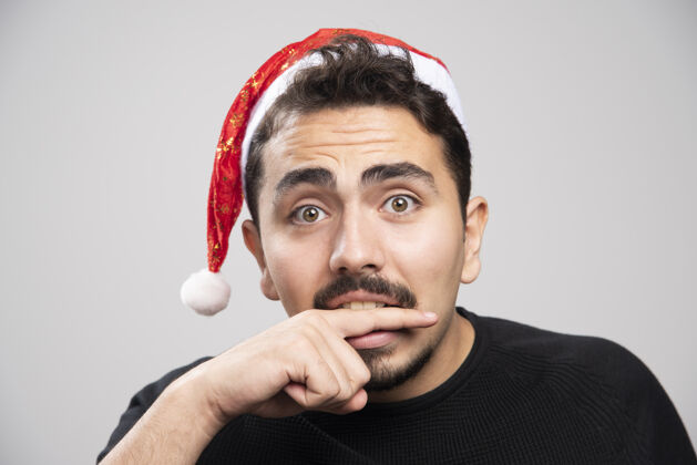 帽子戴圣诞老人帽子的年轻人咬着他的手指男人胡须胳膊