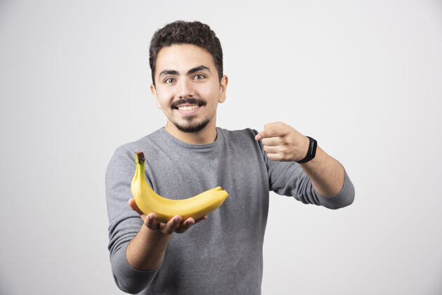 微笑黑发男人拿着香蕉指着它男性表演情绪