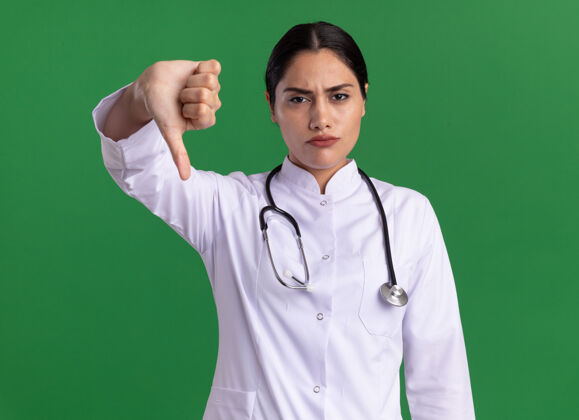 医生年轻的女医生 穿着医用外套 手持听诊器 正脸朝下 站在绿色的墙上听诊器拇指下摆