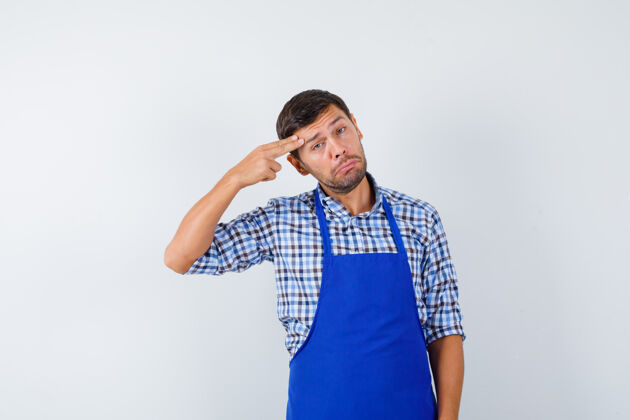 烹饪穿着蓝色围裙和衬衫的年轻男厨师年轻成人厨师