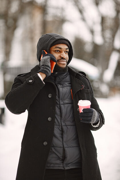 男冬天小镇上的男人穿黑外套的男人拿着咖啡和电话的男人年轻外面男