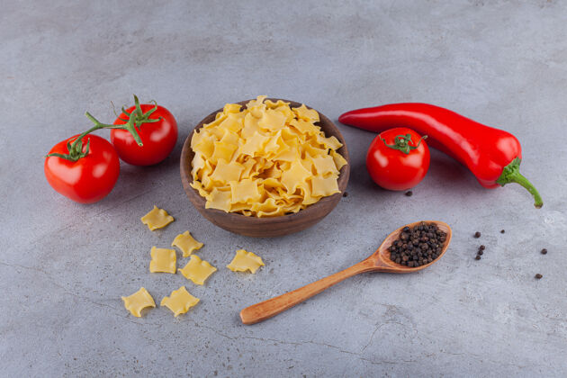 俯视图一个木制的碗 里面装满了生的意大利饺子 还有新鲜的西红柿和辣椒团体自然生的