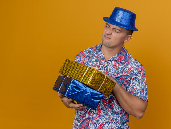 盒子一个未出柜的年轻人 戴着蓝色帽子 拿着礼品盒 在橙色的背景上 留着复印空间壁板抱穿