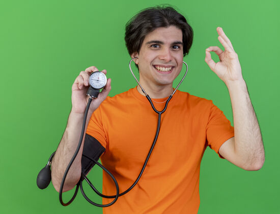 握持微笑的年轻病人戴着听诊器 手持血压计 在绿色背景上显示出良好的姿势微笑佩戴听诊器