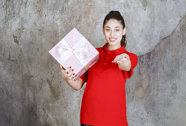 介绍年轻女子拿着一个用白丝带包着的粉红色礼盒 叫前面的人来送礼物人姿势邀请